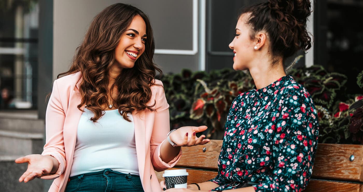Two women sitting on a bench, smiling and talking